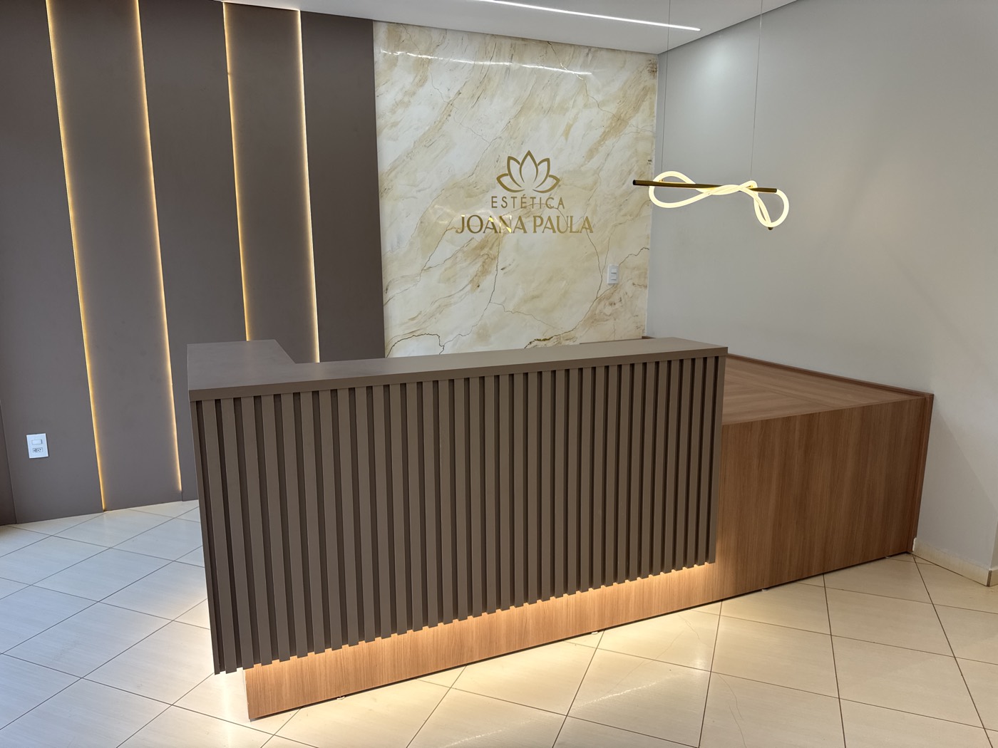 Recepção da Estética Joana Paula, com balcão de madeira e logo dourado no mármore
